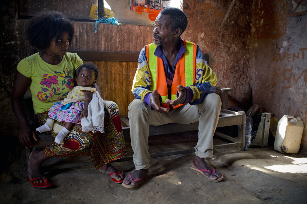 A woman holds a baby while speaking to a man