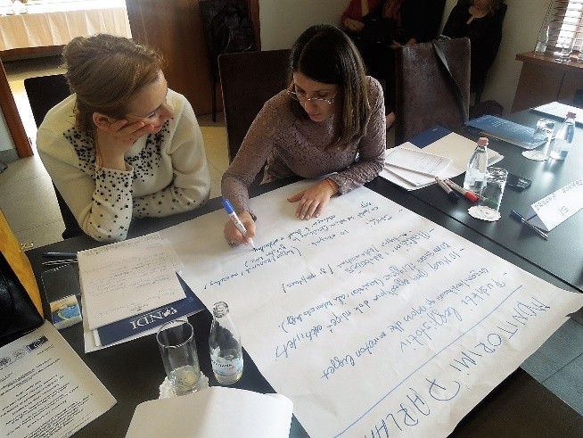 Two women write on a white poster board