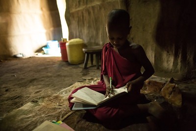 Teresia Oloitai's son studying inside their home. Because of electricity provided by Power Africa he can now study at night with lightbulbs