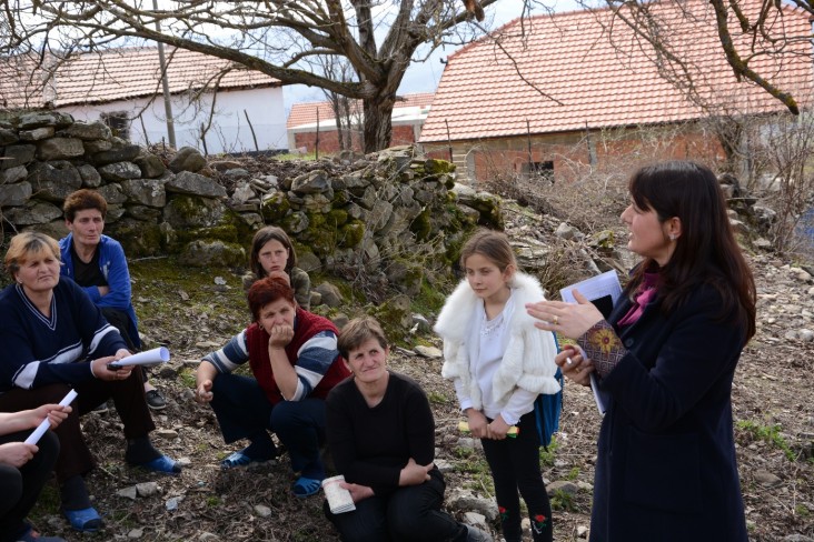 Woman speak in front of a group of women sitting in an outdoor field