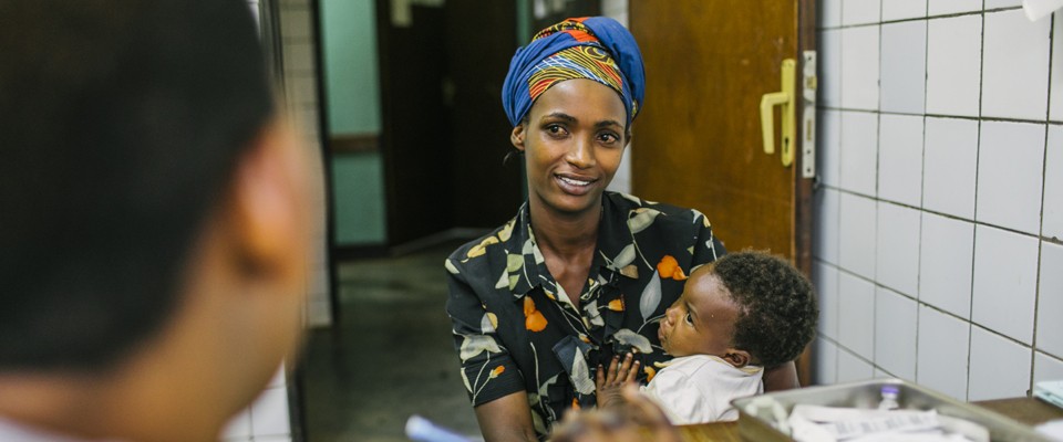 A mother holds her baby while speaking to a health care worker