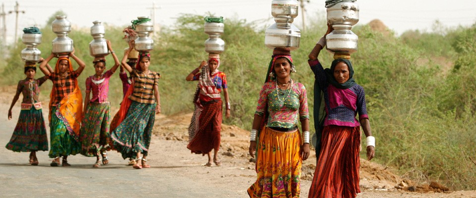 A group of women walk along a road carrying goods