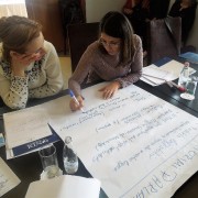 Two women write on a white poster board