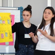 A young woman speaks in front of a yellow poster board