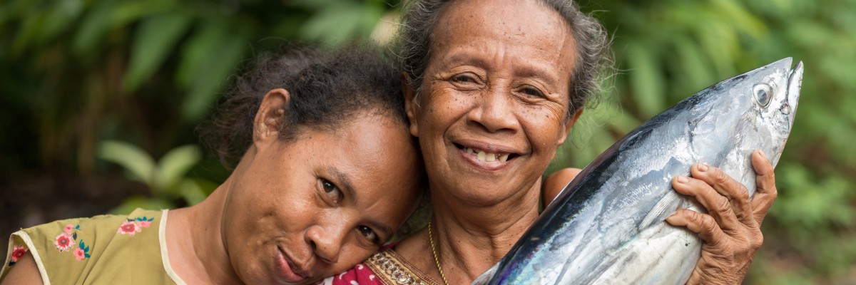 Ibu-ibu berseri-seri menunjukkan ikan tongkol segar di Banda Neira, Pulau Maluku.