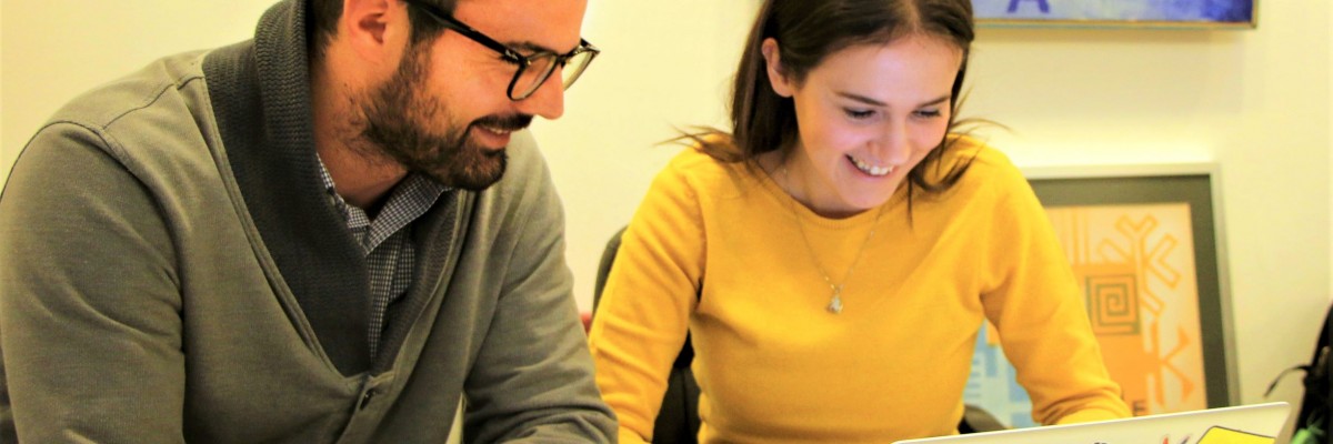 A man and a woman look at a laptop